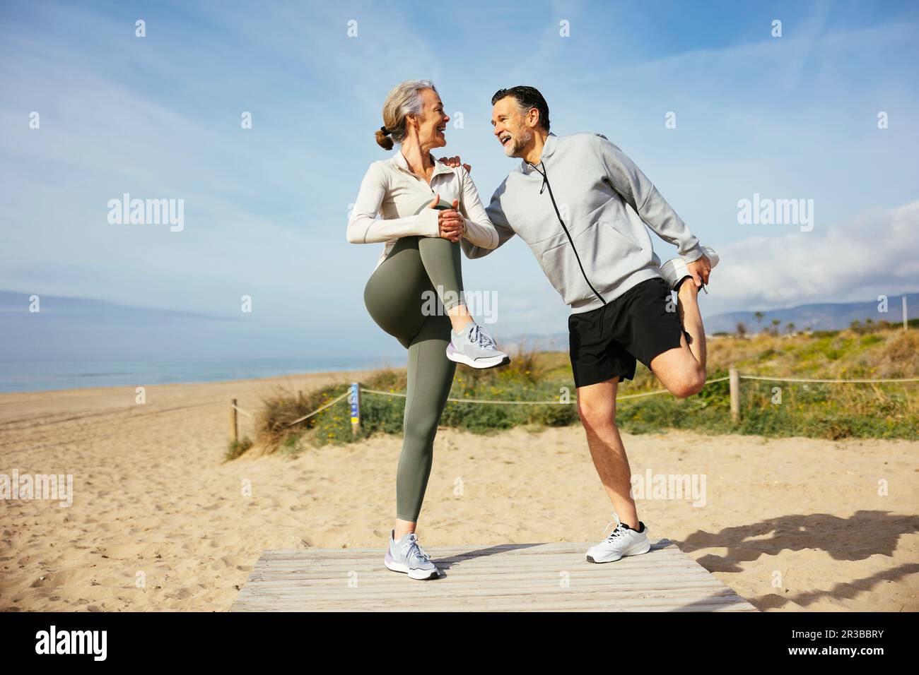 Glückliches, reifes Paar, das sich am Strand die Beine streckt Stockfoto