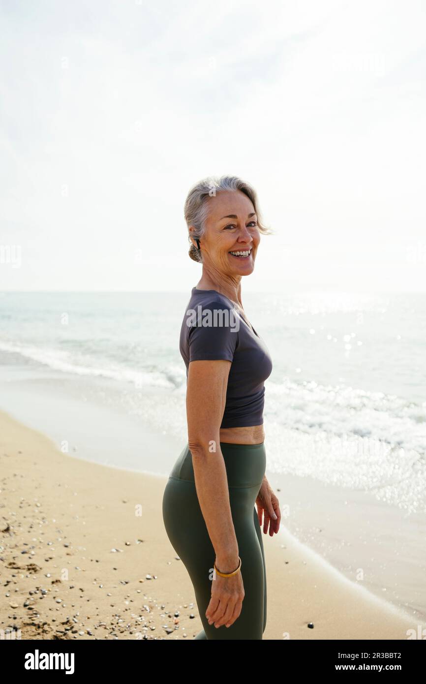 Lächelnde reife Frau, die am Strand steht Stockfoto