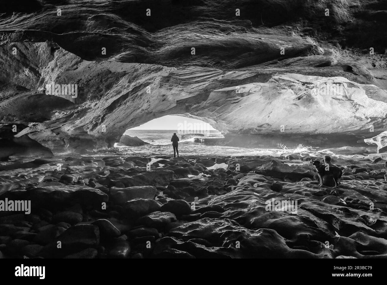 Im Inneren der Waenhuiskrans Cave bei Arniston in der Provinz Westkap. Menschen und ein Hund sind sichtbar. Schwarzweiß Stockfoto