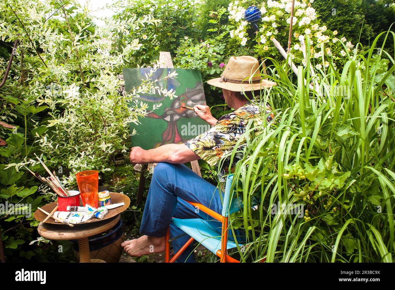 Ein Mann malt inmitten von Pflanzen, sitzt auf einem Stuhl im Garten Stockfoto