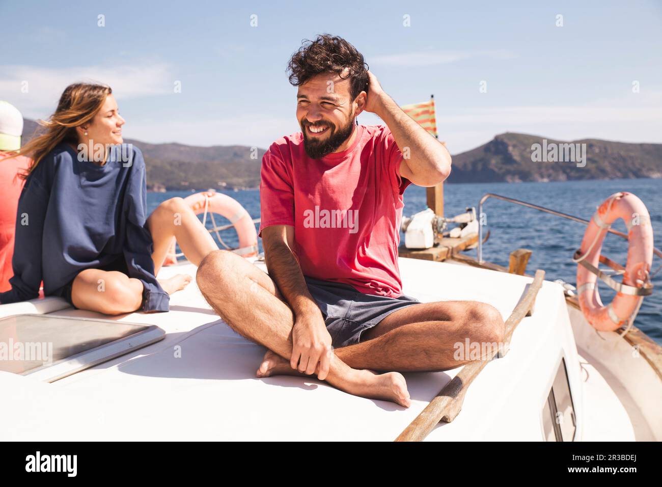 Ein lächelnder Mann, der im Urlaub mit einer Frau auf einer Jacht im Kreuzbein sitzt Stockfoto