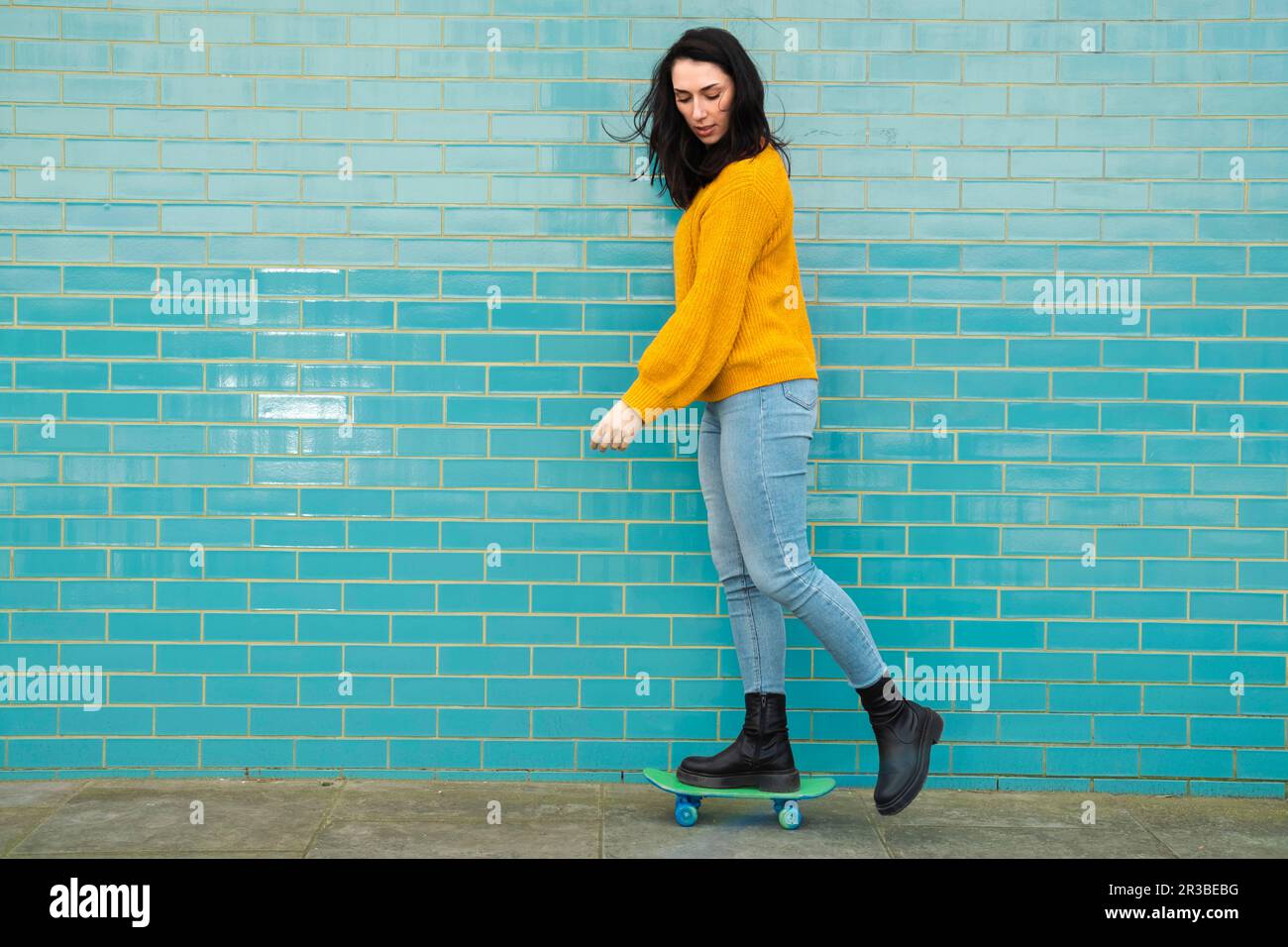 Junge Frau in legerer Kleidung, Skateboarden vor türkisfarbenen Wänden Stockfoto