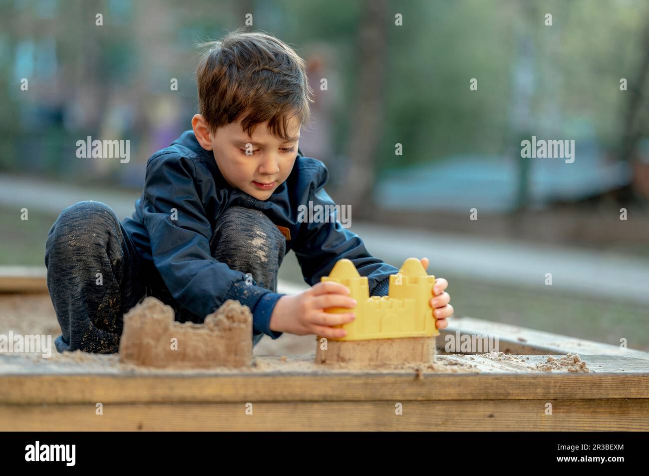Ein Junge baut eine Sandburg mit Spielzeug im Park Stockfoto