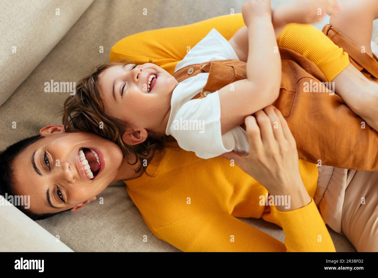 Fröhliche Frau, die ihren Sohn zu Hause auf dem Sofa kitzelt Stockfoto