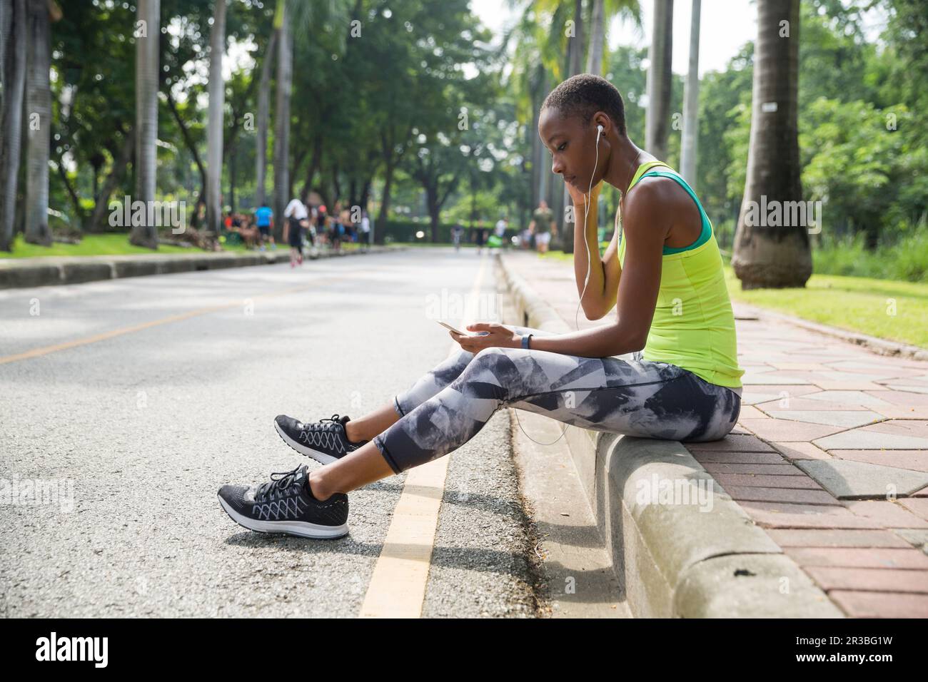 Eine Frau, die Musik hört, sitzt auf dem Bürgersteig im Park Stockfoto