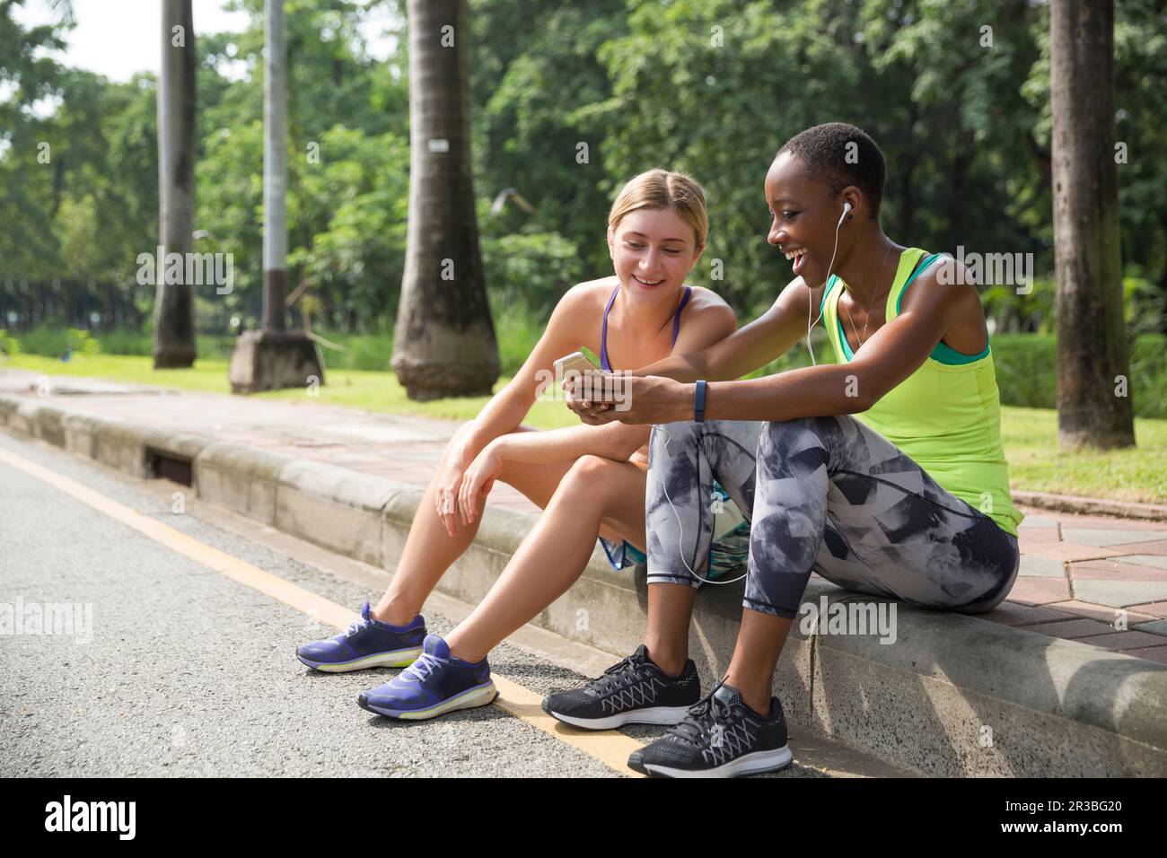 Fröhliche Freunde, die ihr Smartphone auf dem Bürgersteig im Park teilen Stockfoto