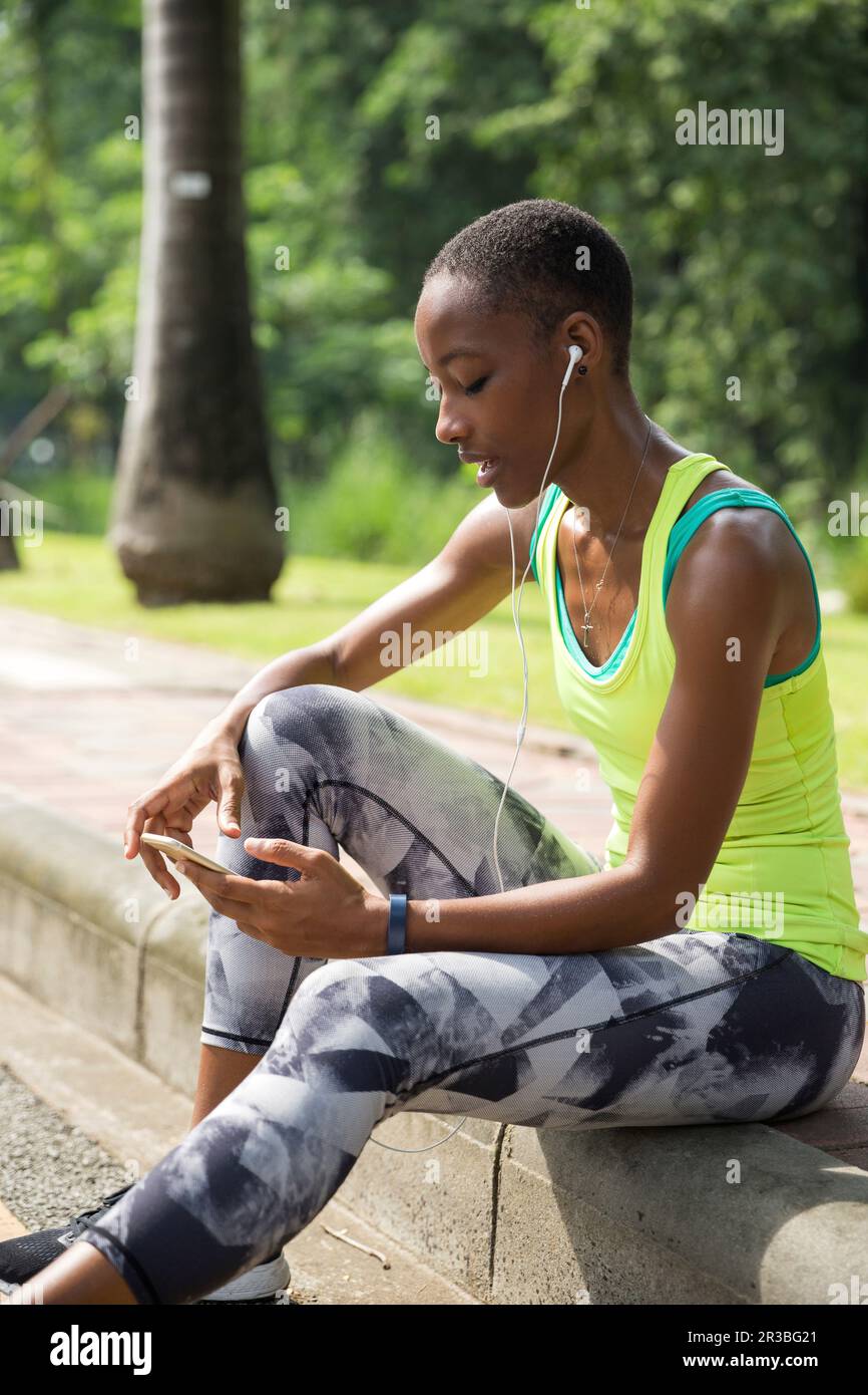 Eine Frau, die im Netz durch ein Smartphone surft und auf dem Bürgersteig im Park sitzt Stockfoto