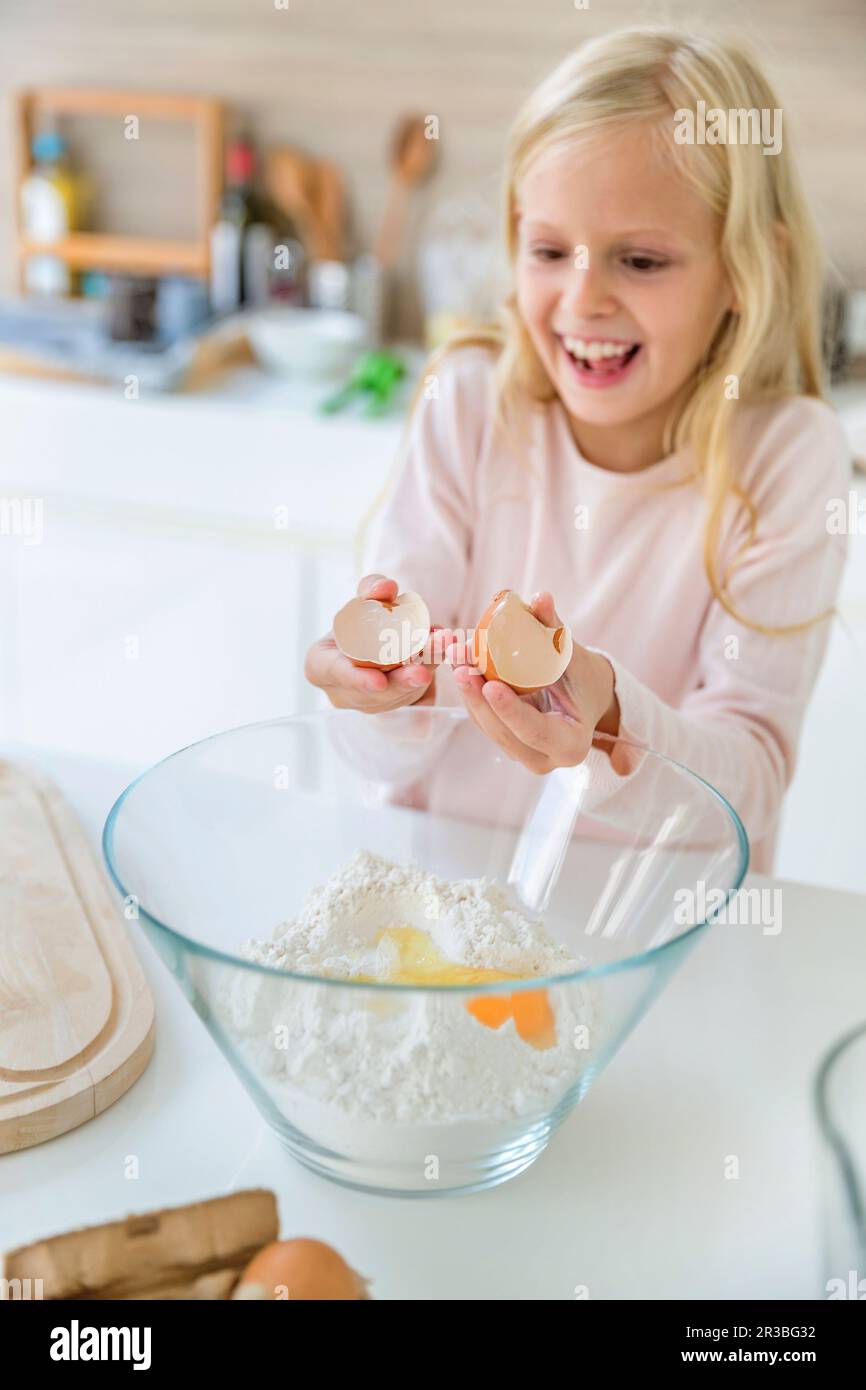 Glückliches Mädchen, das zu Hause Eier in Mehl zerbricht Stockfoto