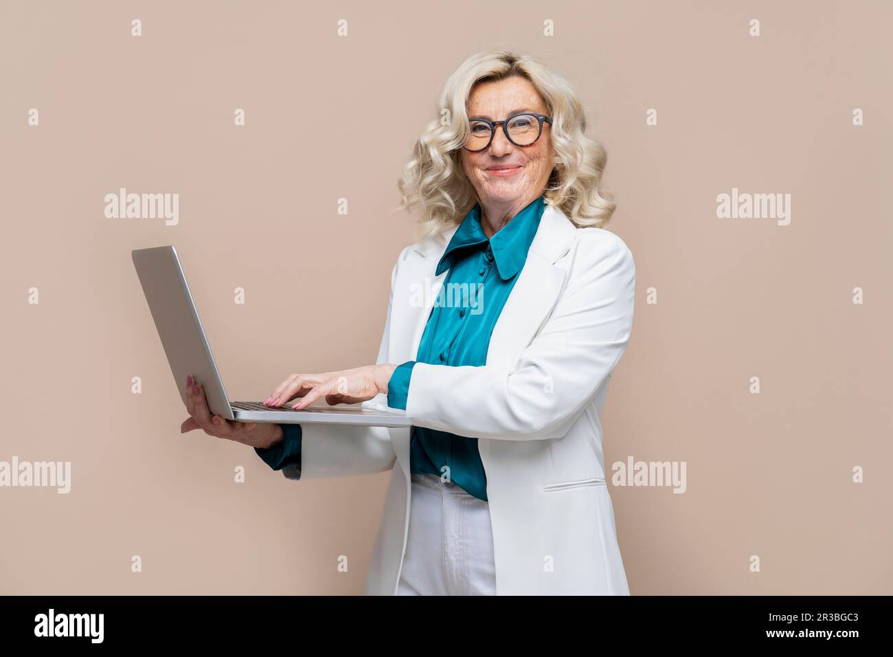 Lächelnde ältere Geschäftsfrau, die den Laptop vor einem farbigen Hintergrund hält Stockfoto