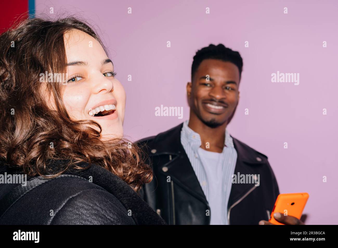 Glückliche Frau mit einem Mann, der im Hintergrund ein Smartphone hält Stockfoto