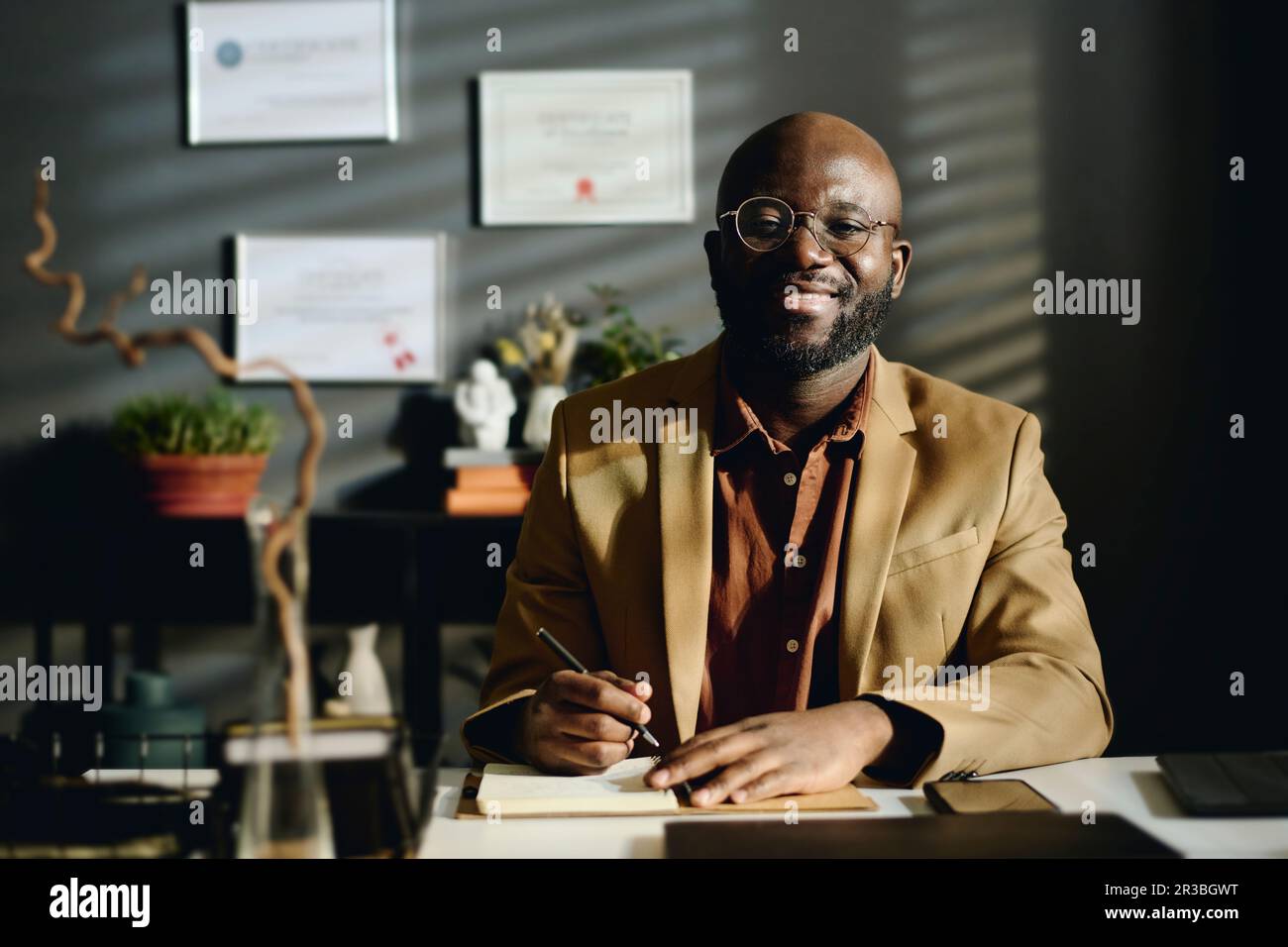Lächelnder Psychologe mit Blazer am Schreibtisch im Büro Stockfoto