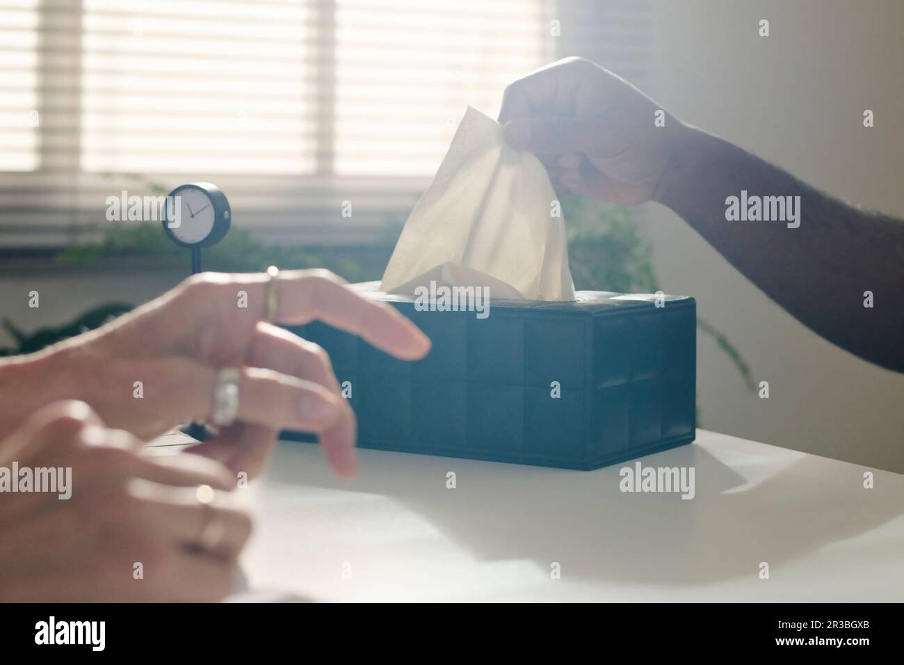 Hand eines Patienten, der am Schreibtisch in der Praxis eine Papierserviette aus der Schachtel zieht Stockfoto