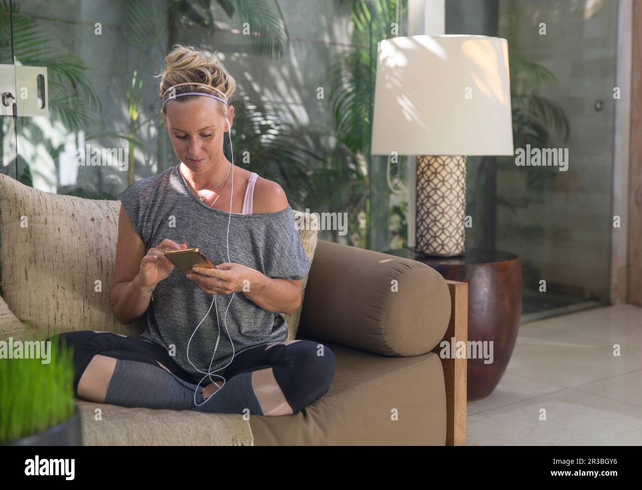 Frau mit in-Ear-Kopfhörern, die zu Hause auf dem Sofa sitzt und ein Smartphone verwendet Stockfoto