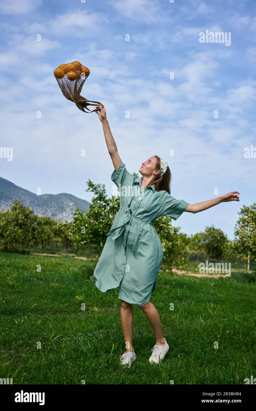Verspielte Frau mit Netztasche im Orangengarten Stockfoto