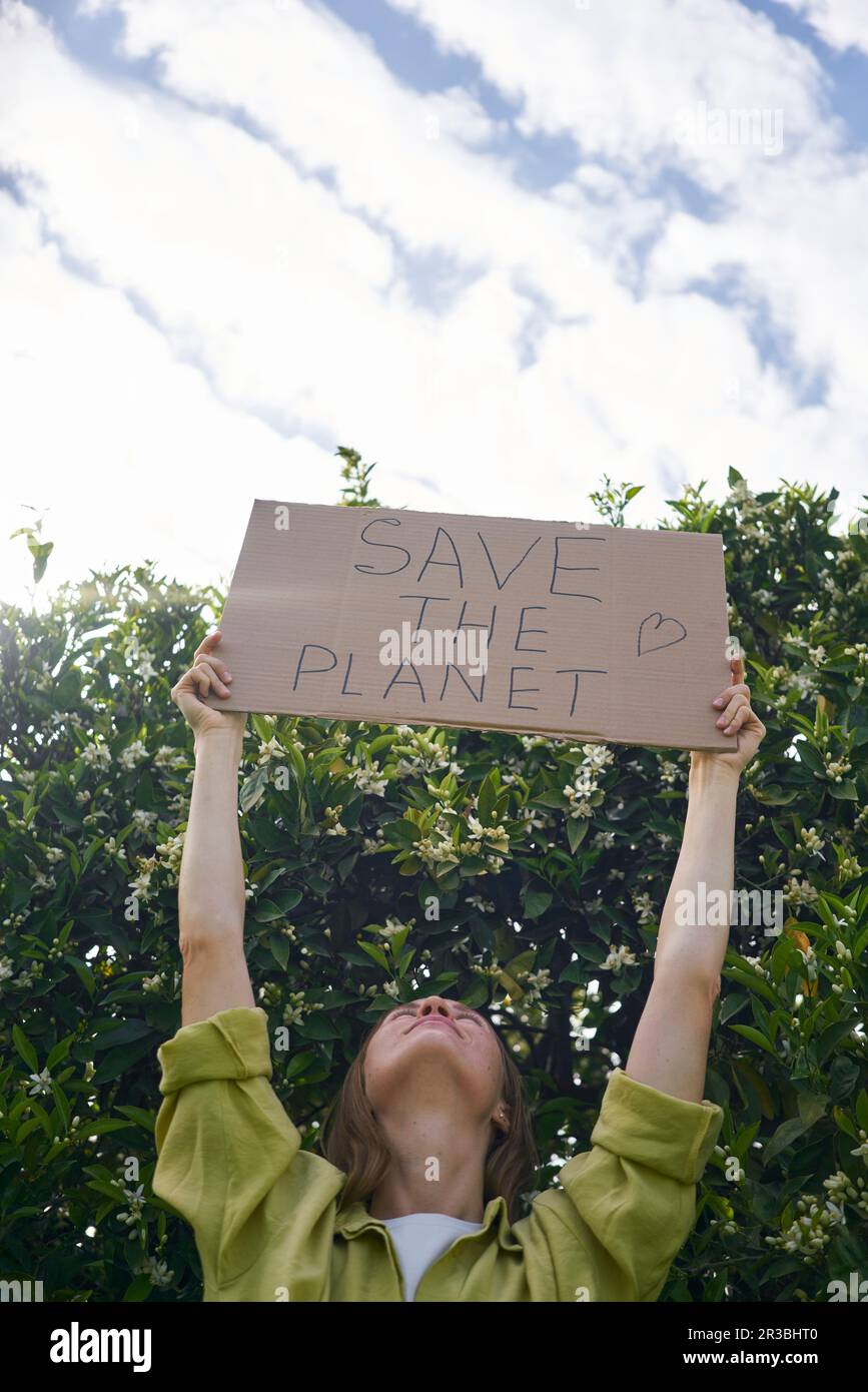 Eine Frau, die Pappe in der Hand hält, ausgeschnitten mit „Save the Planet“-Text neben dem Baum im Garten Stockfoto