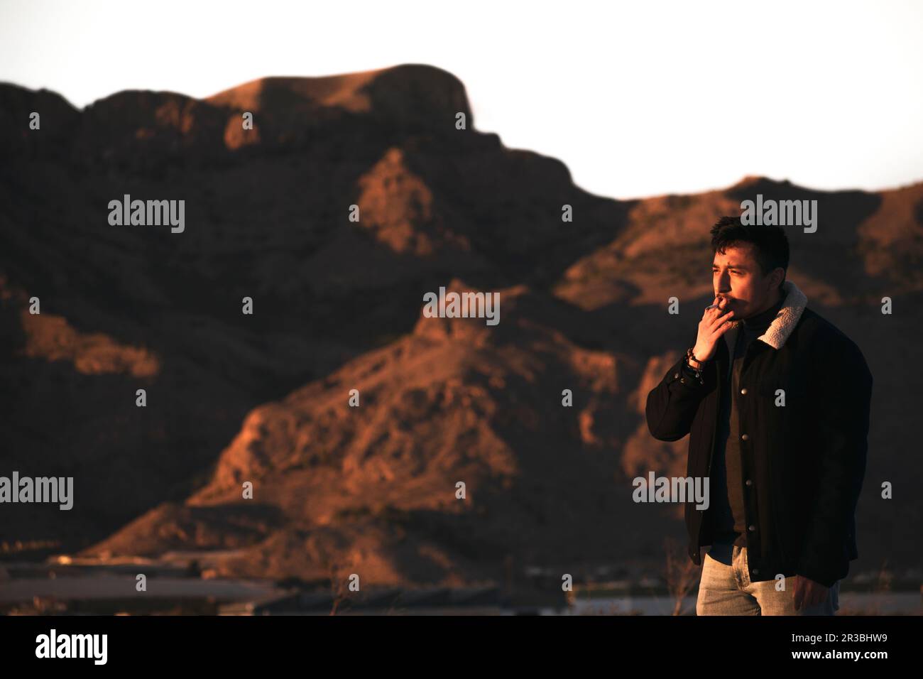 Junger Mann, der bei Sonnenuntergang in der Nähe der Berge raucht Stockfoto