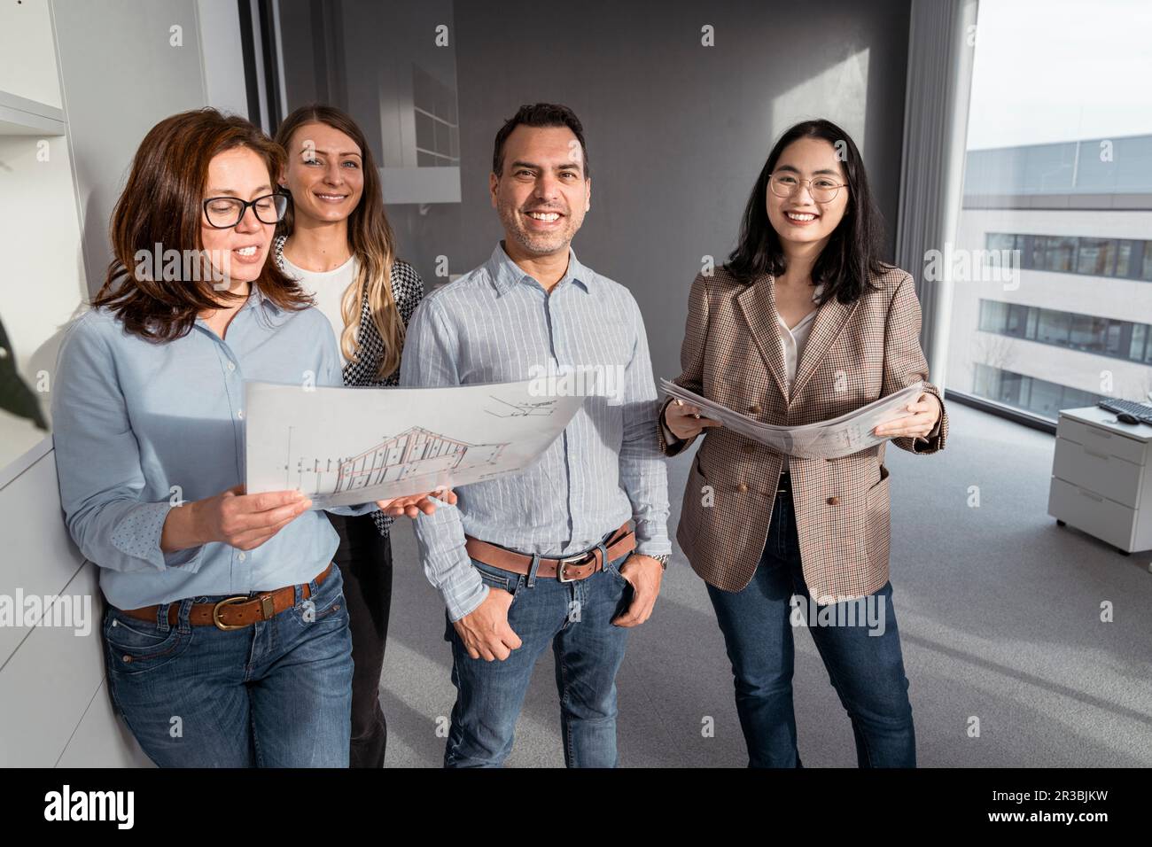 Selbstbewusste Geschäftsleute, die im Büro stehen und Architekturpläne haben Stockfoto