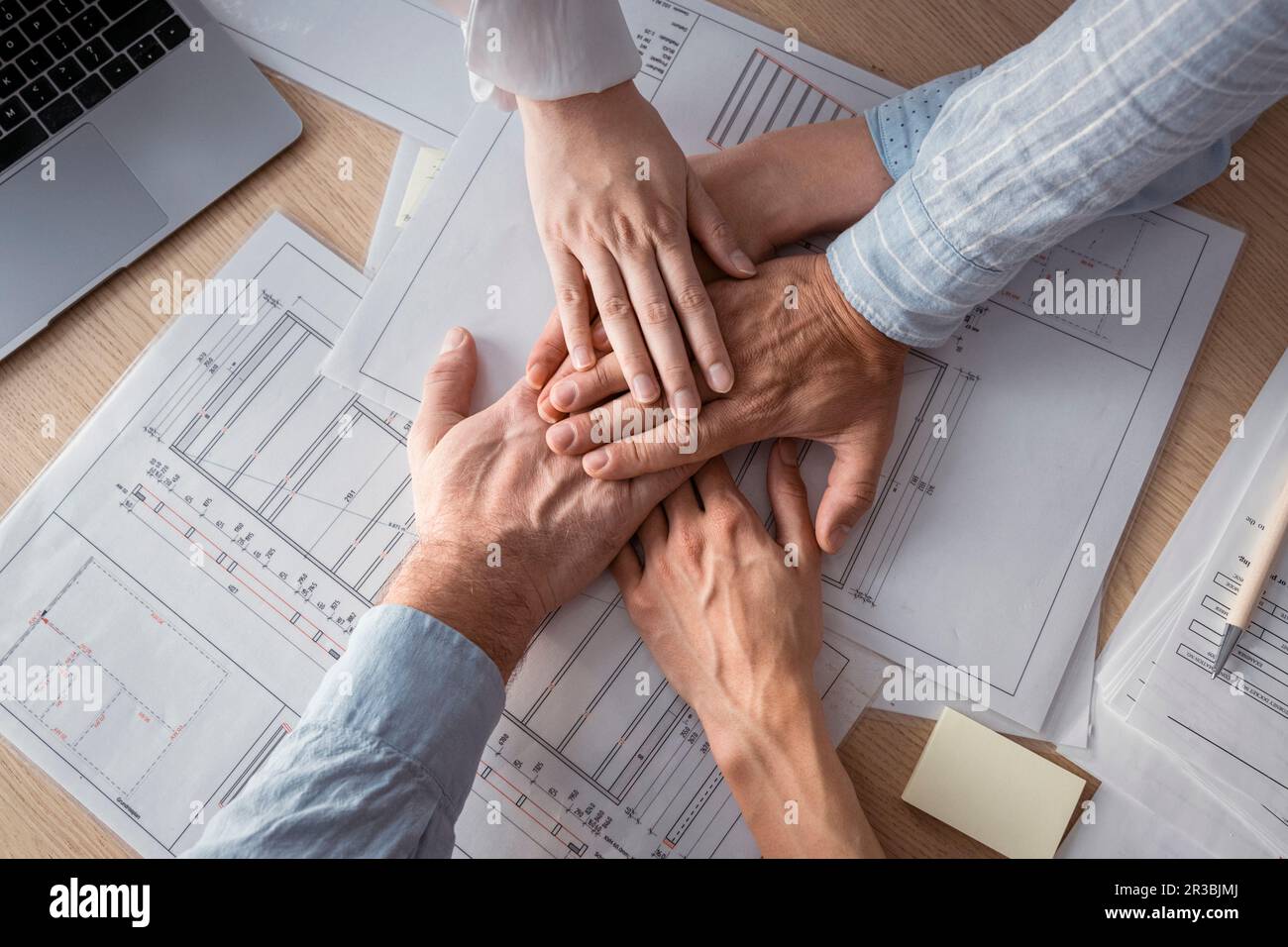 Geschäftsleute, die Hände auf dem Schreibtisch mit Architekturplänen stapeln Stockfoto