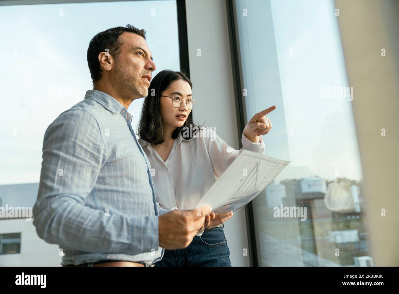Geschäftsmann und Geschäftsfrau mit architektonischem Plan und Blick aus dem Fenster Stockfoto