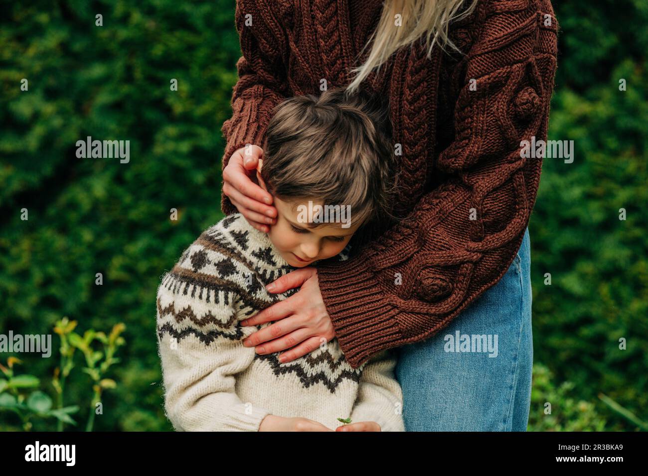 Mutter im braunen Pullover umarmt Sohn im Garten Stockfoto