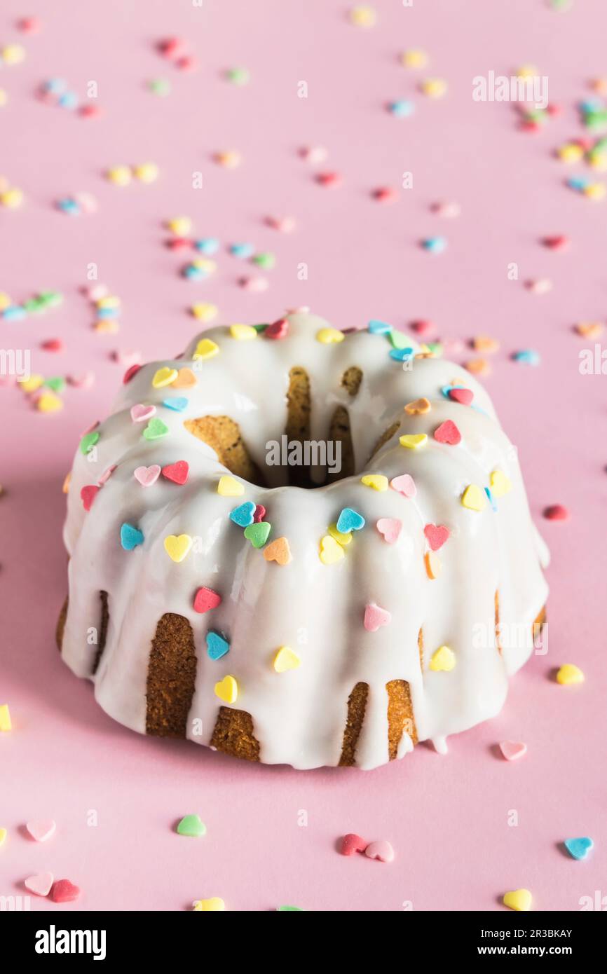 Bundt-Kuchen mit weißer Glasur und farbenfrohen herzförmigen Zuckerstreuseln zum Valentinstag Stockfoto