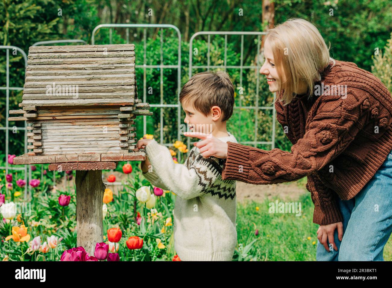 Neugieriger Sohn, der durch die Mutter im Garten ins Vogelhaus schaut Stockfoto