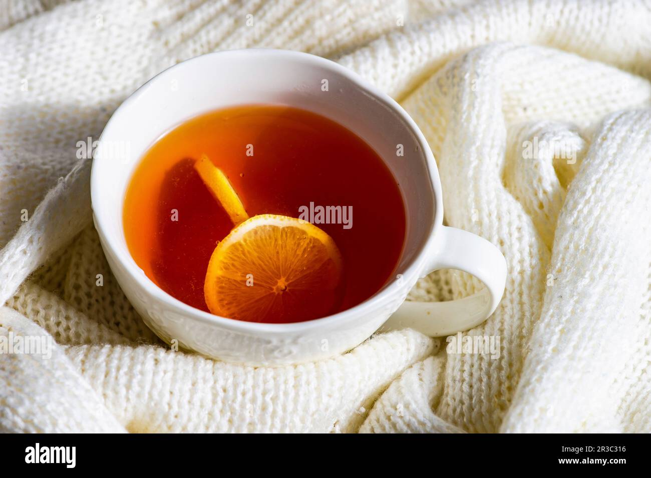 Eine Tasse heißer Tee mit Zitronen- und weißem Strickpullover als Winterkonzept Stockfoto