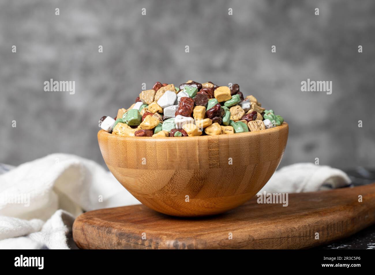 Bunte Schokoladensteine. Schokoladendragee aus Stein in Holzschüssel auf dunklem Hintergrund. Kleine mehrfarbige Süßigkeiten Stockfoto