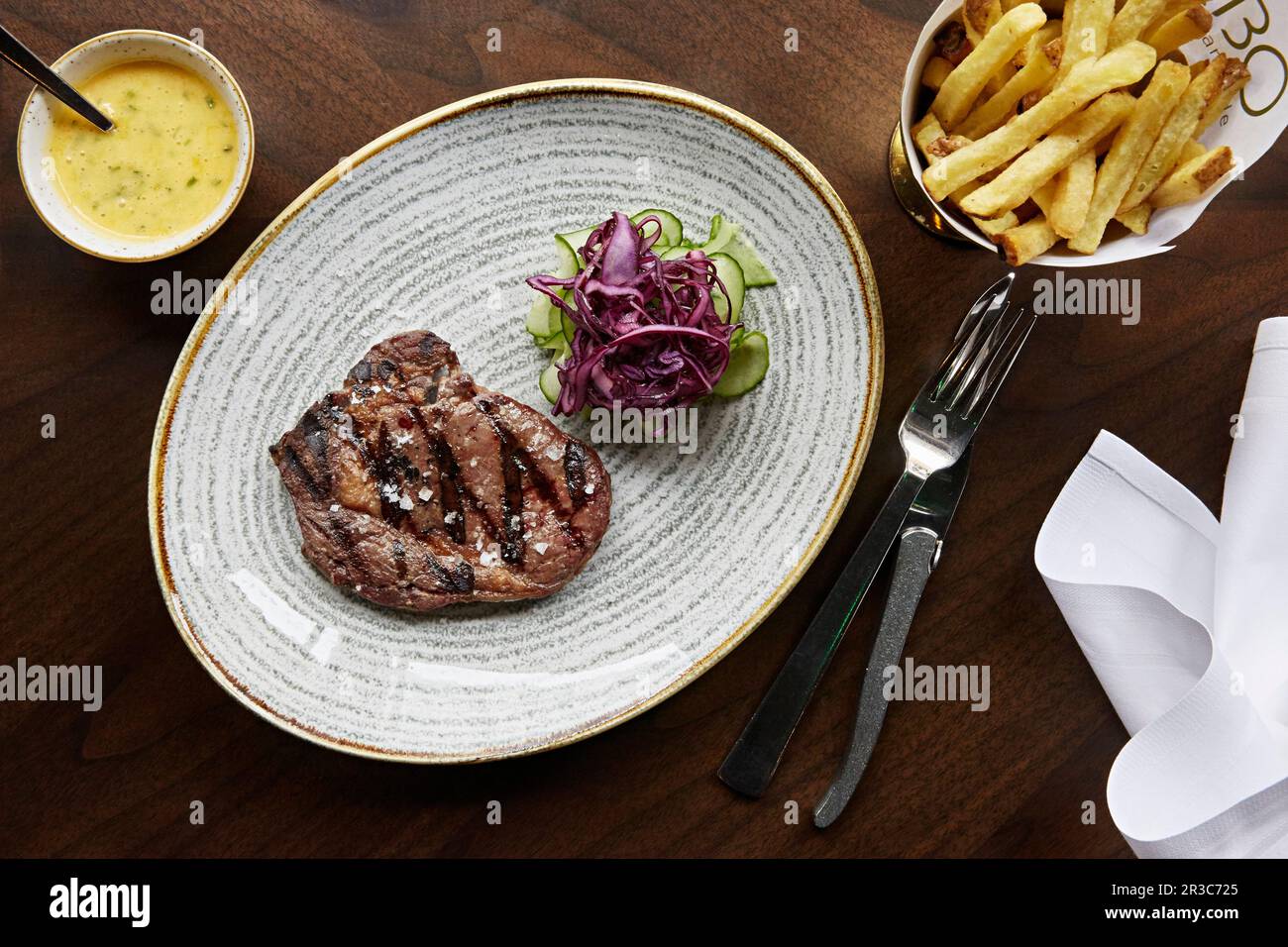 Ein Steak mit Meersalz und einer Seite eingelegter Gurken, lila Kohl und Pommes Stockfoto