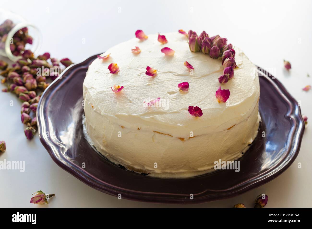 Rosenkuchen mit getrockneten Rosenknospen und Blütenblättern auf einem violetten Teller Stockfoto