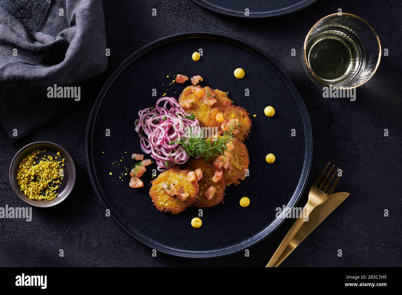 Kleine Lachskuchen mit Zwiebelsalat auf schwarzem Teller, mit goldenem Besteck Stockfoto