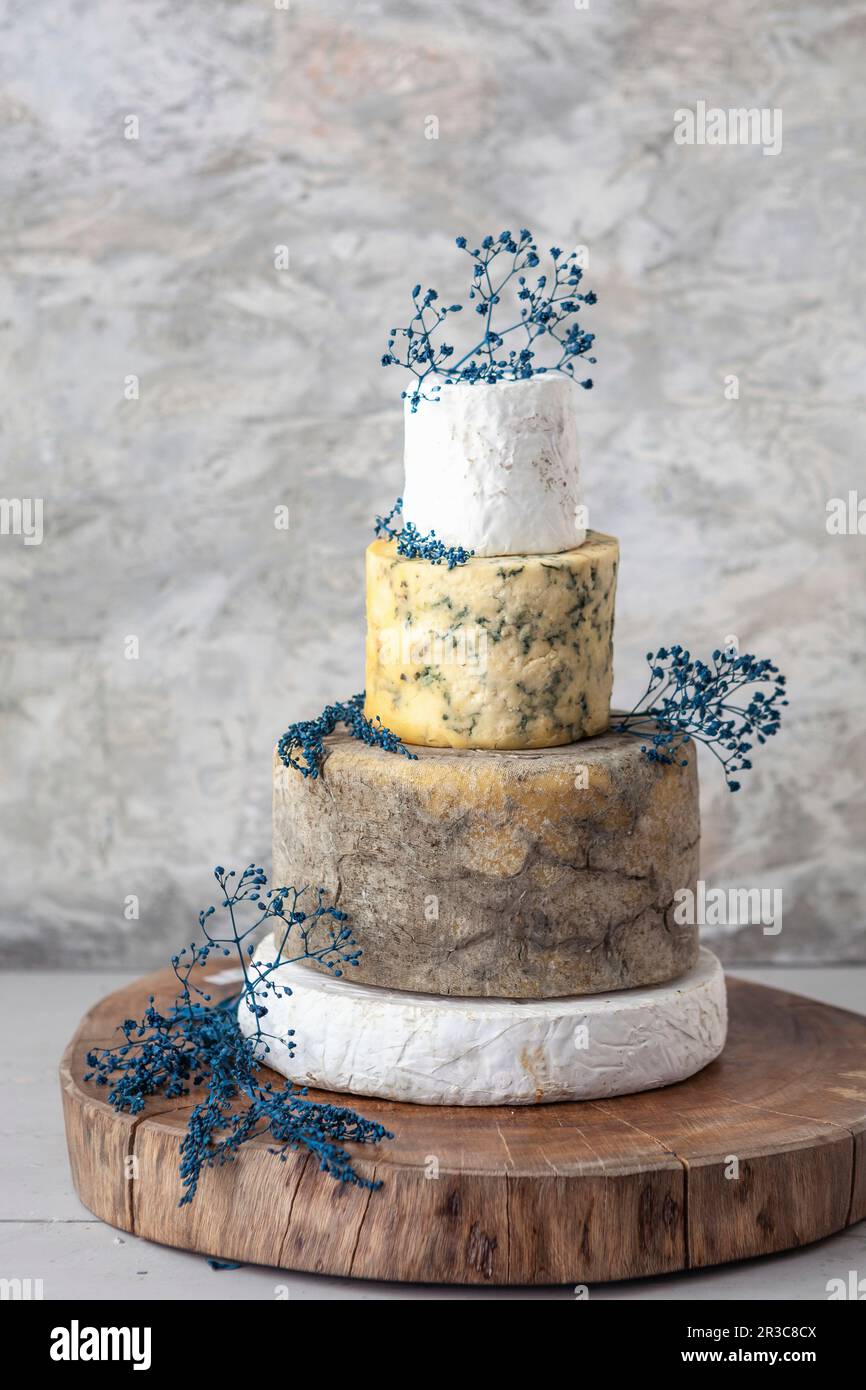 Cheese Wedding Cake – Käsekuchen, die als mehrstufige Hochzeitstorte mit Blumen angeordnet sind Stockfoto
