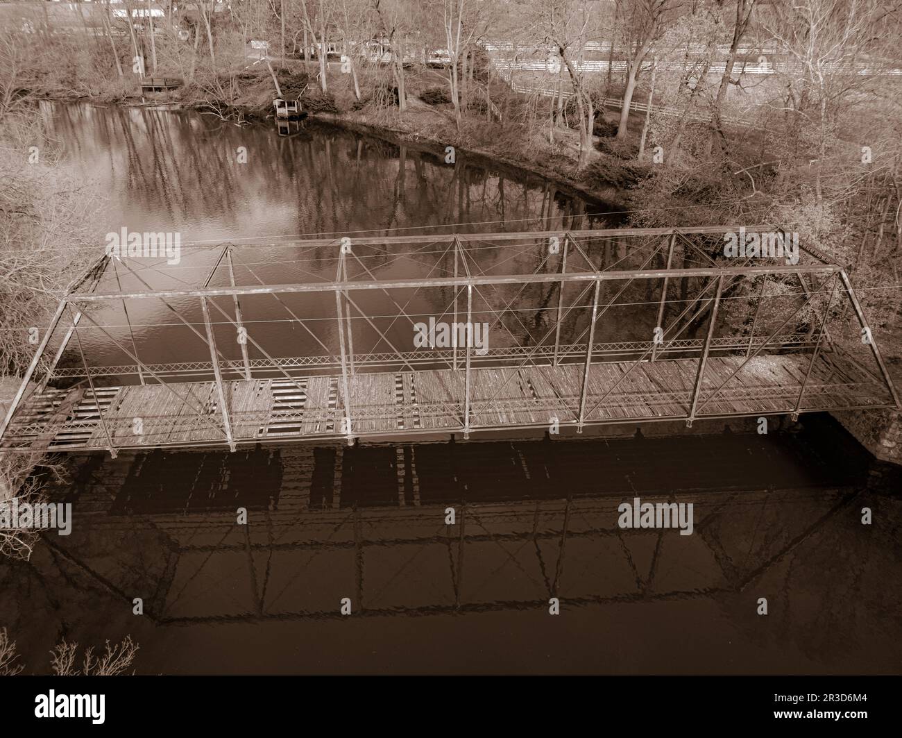 Eine Reise durch die Zeit in Sepiatönen: Eine alternde Brücke über einen ruhigen Fluss, umgeben von warmen Farbtönen, ruft Nostalgie und ein zeitloses Gefühl der Geschichte hervor. Stockfoto