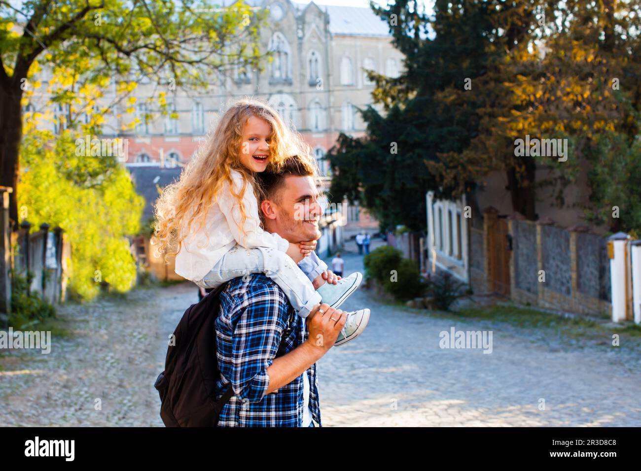 Der junge Vater trägt seine kleine Tochter auf seinen Schultern. Verspielte Männer und Mädchen laufen durch die Altstadt Stockfoto