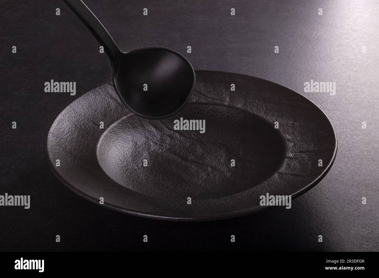 Trendiges Design Küchenzubehör, schwarze Platte und Kelle auf dunklem Hintergrund. Stockfoto