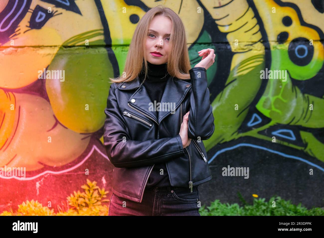 Junge blonde Frau neben der Graffiti-Wand. Straßenkunst und zeitgenössische Malerei. Straßenleben. Stockfoto