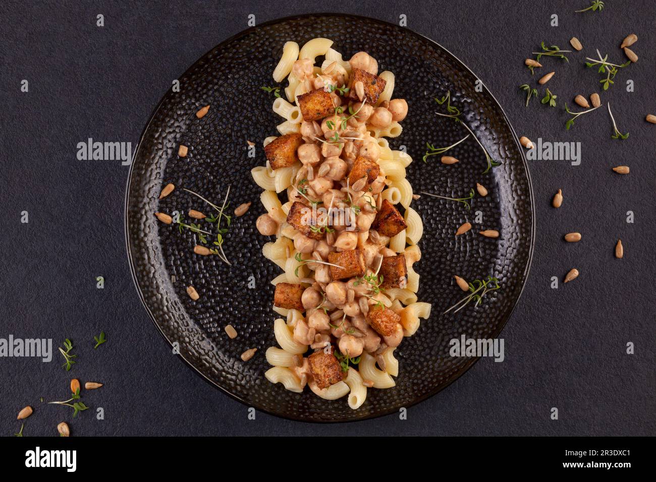 Leckere Pasta mit Kichererbsen, Tofu und frischen Kräutern auf dunklem Hintergrund von oben. Stockfoto
