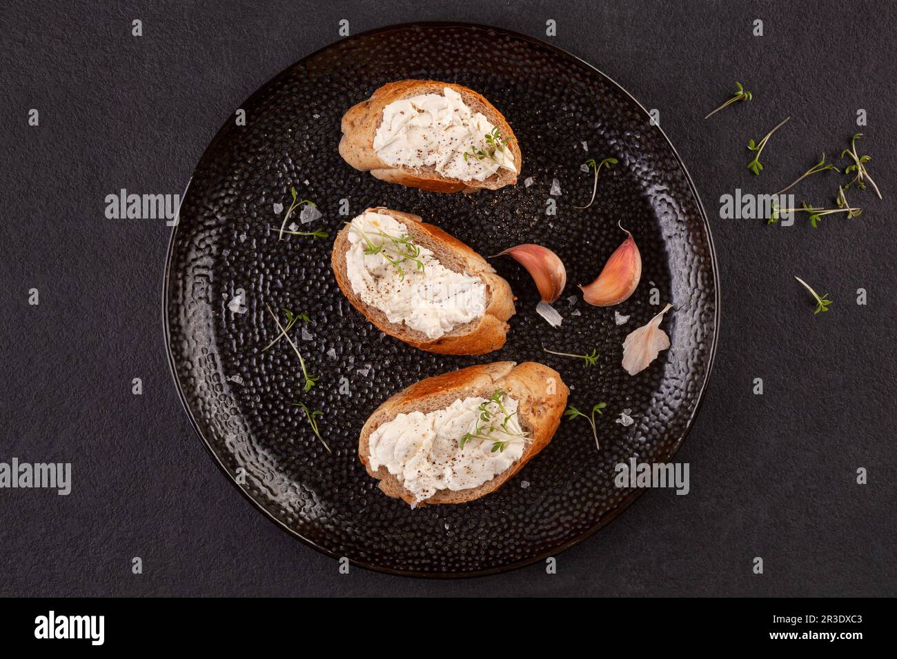 Flache Laienzusammensetzung mit Brot und Knoblauch auf schwarzer Platte. Stockfoto