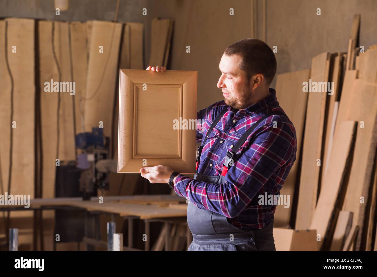 Der Zimmermann in Arbeitskleidung sieht sich ein eigenes Produkt an Stockfoto