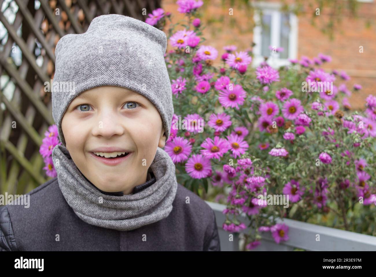 Seltsamer Junge mit einem Lächeln im Mantel neben Blumen Stockfoto