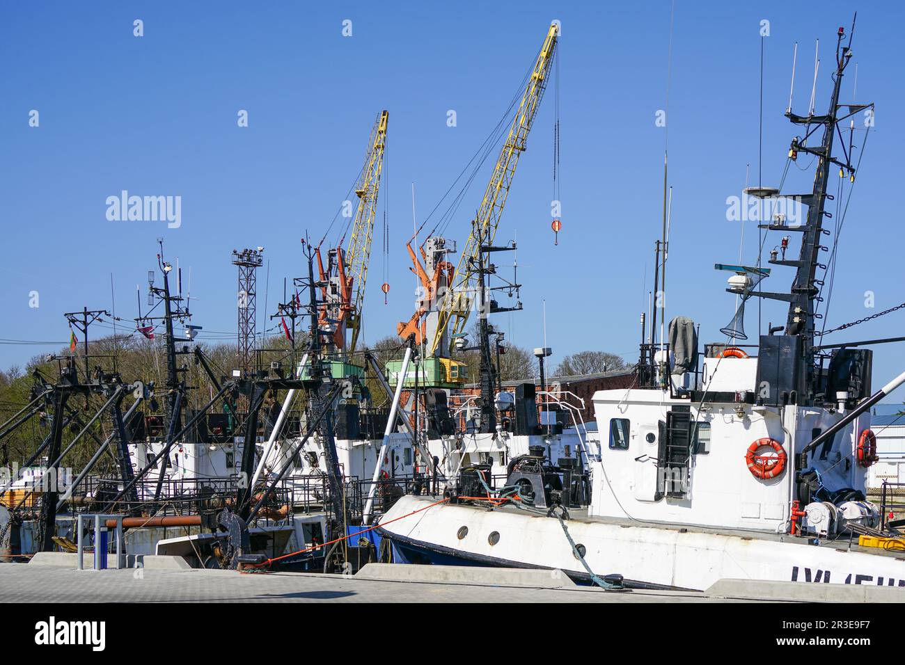 Farbenfroher Blick auf den Hafenpier mit kleinen Fischereifahrzeugen und Hafenkranen im blauen Hintergrund, Liepaja, Lettland, Ostsee Stockfoto