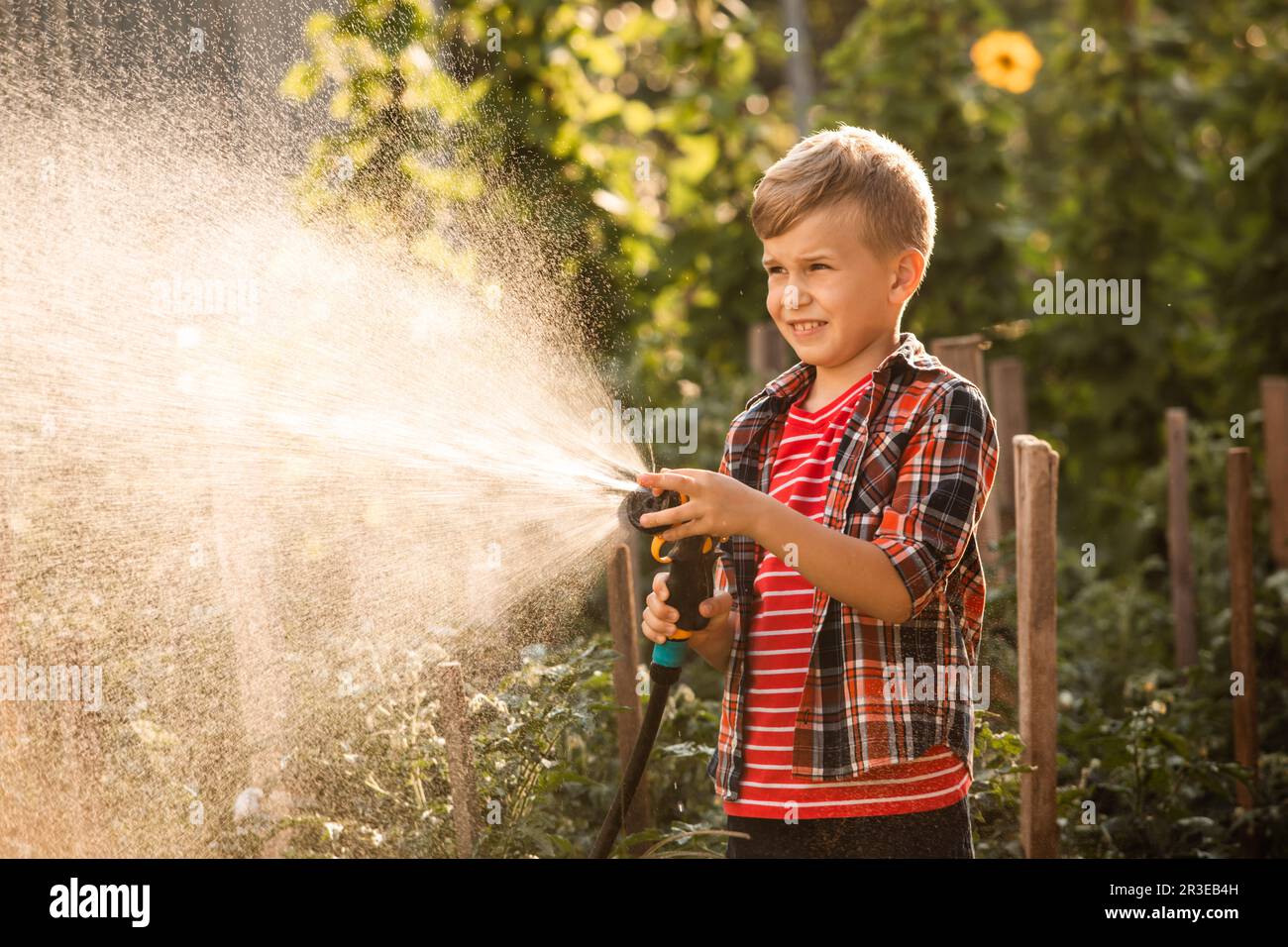 Der kleine Junge wäscht die Pflanzen und macht große Wasserspritzer Stockfoto