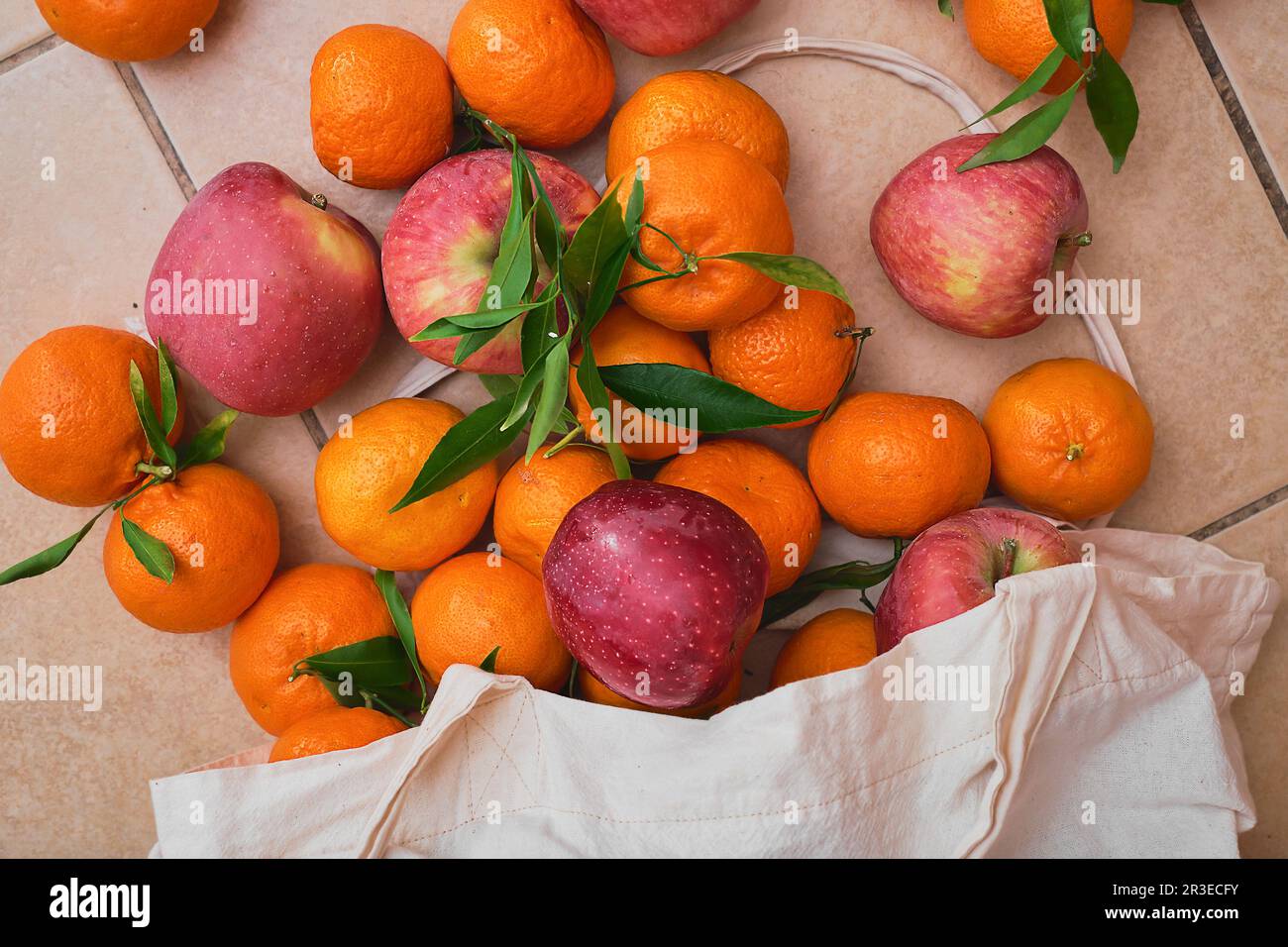 Rote Äpfel und Mandarinen in einem wiederverwendbaren Öko-Beutel auf Keramikboden. Obstlieferung vom Bauernmarkt, gesunde Lebensmittel. Blick von oben auf saftige Früchte. Stockfoto