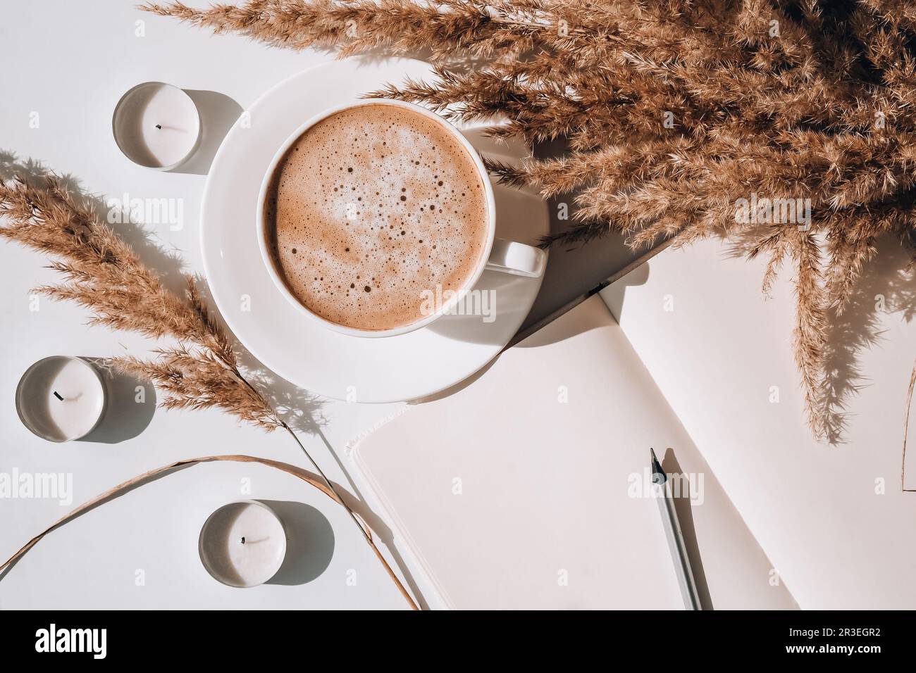 Pampas-Gras und weiße Tasse mit Kaffee. Leeres Notizbuch, das einen Plan für den Tag macht. Cappuccino trinken am Morgen a Stockfoto