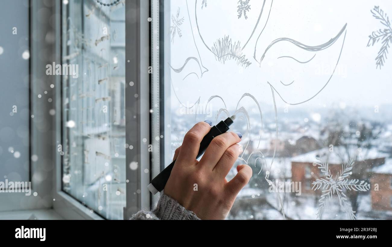 Weibliche Hand Malerei Weihnachtshirsch auf Fensterglas gemalt. Weihnachtliche Winterdekoration auf dem Fensterglas. Weißes Muster von Hirschen. Snow Art Tracery Windo Stockfoto