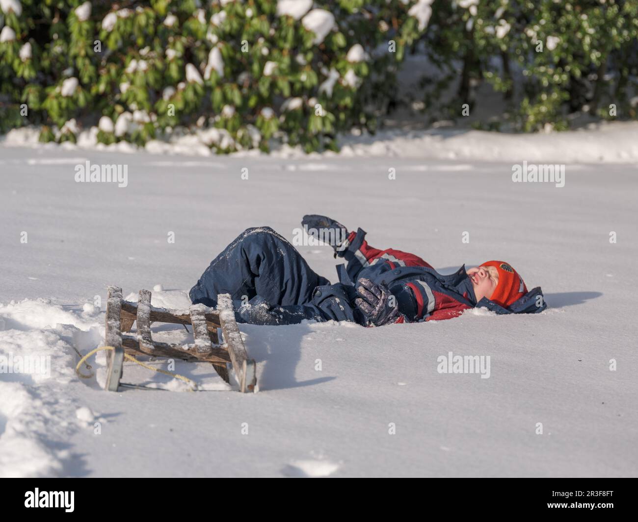 Ein Junge mit Schlitten liegt im Schnee Stockfoto