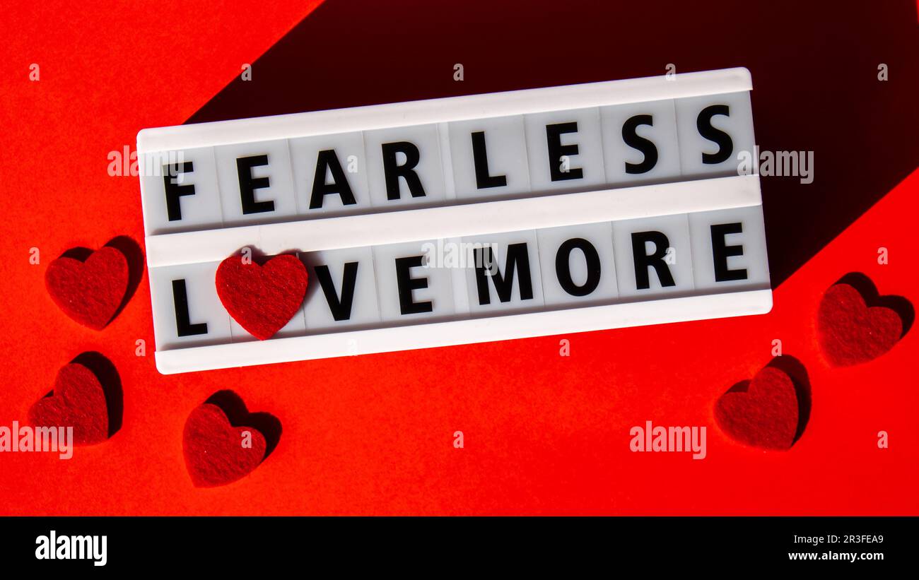 Lightbox mit Text FÜRCHTET WENIGER LIEBE MEHR. Motivierende Wörter Zitat Konzept mit roten Herzen. Farbenfroher roter Hintergrund. Minimalistisch Stockfoto