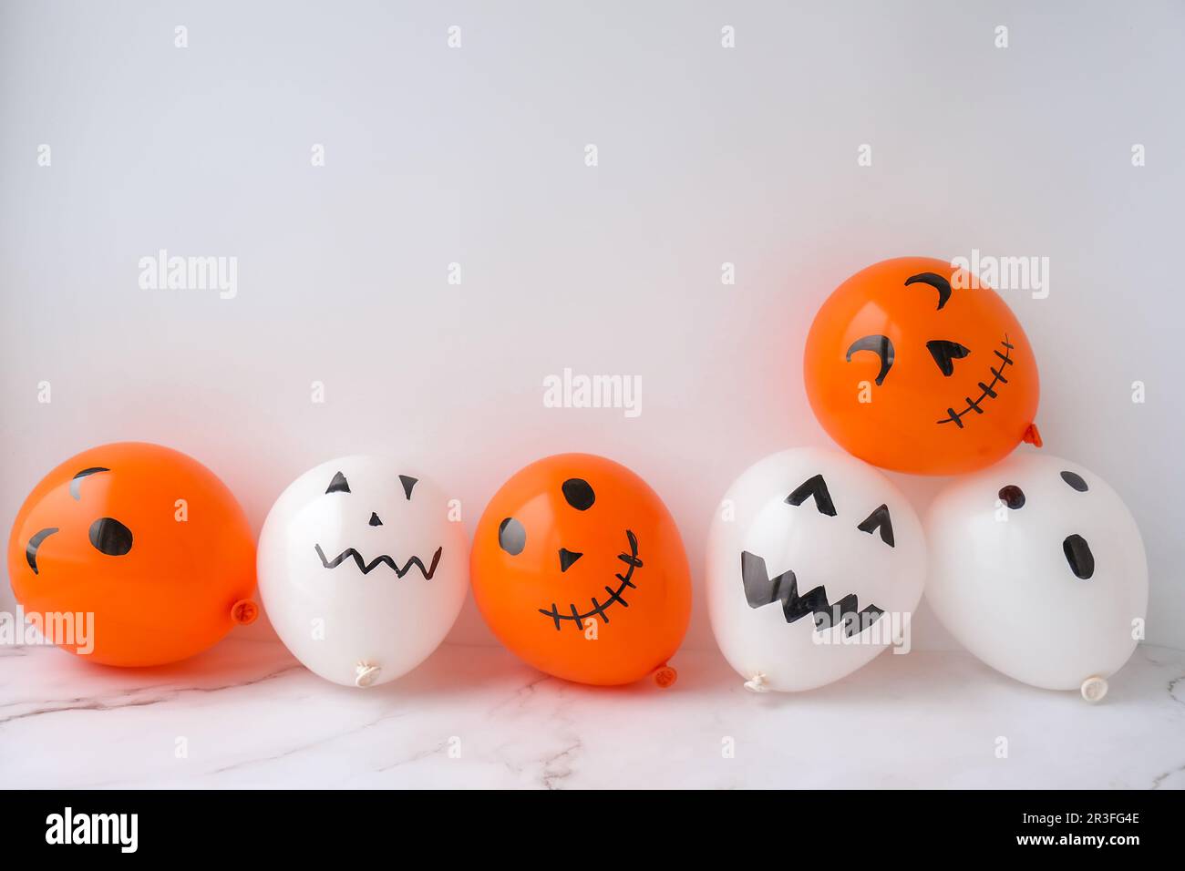 Bemalte Buben auf Ballons. Orangefarbene und weiße Bälle bereiten sie sich selbst für die halloween-Party vor. Halloween-Aktivitäten. Handgefertigt Stockfoto