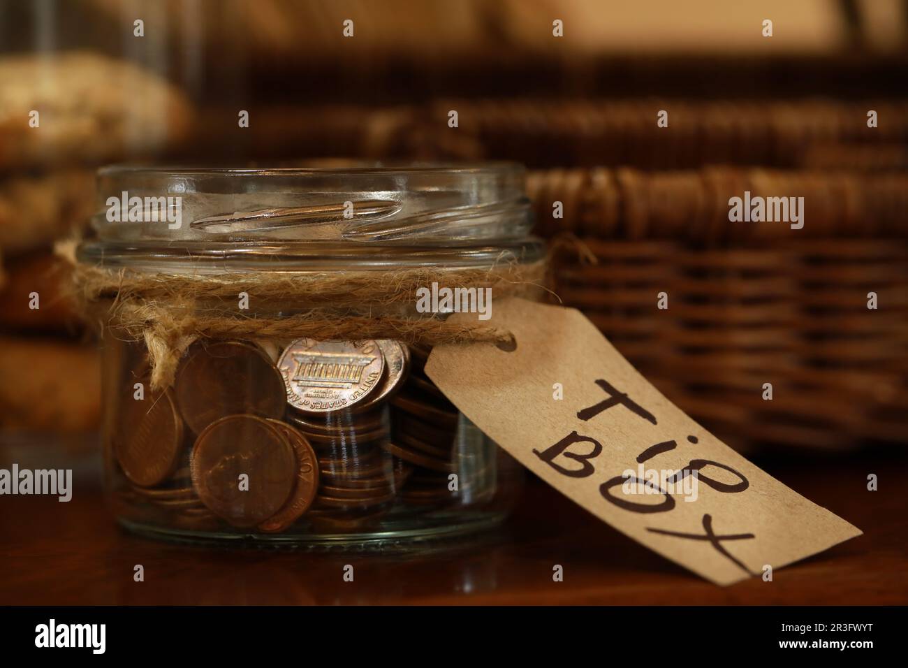 Ein Trinkgeldkasten voll mit Münzen auf einem Holztisch im Café, Schließung Stockfoto