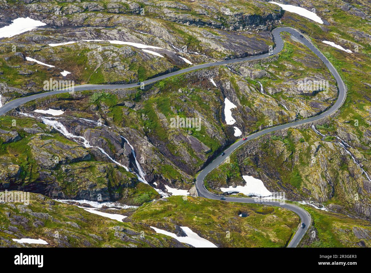 Kurvenreiche Straße in einer grünen Landschaft mit Schneeflecken in Norwegen gesehen Stockfoto